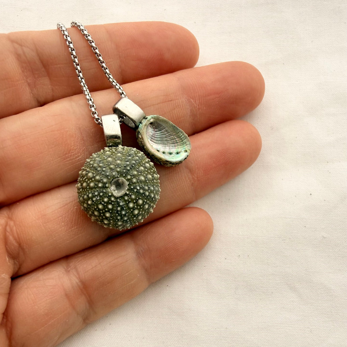 Kina + Pāua (Medium) necklace in silver, shown on a hand