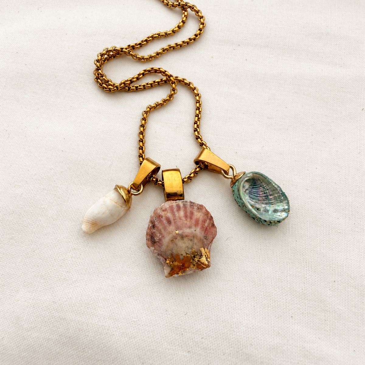 Whelk, scallop and pāua shell trio necklace on light cream fabric