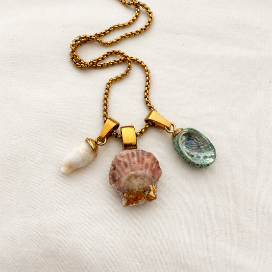 Whelk, scallop and pāua shell trio necklace on light cream fabric